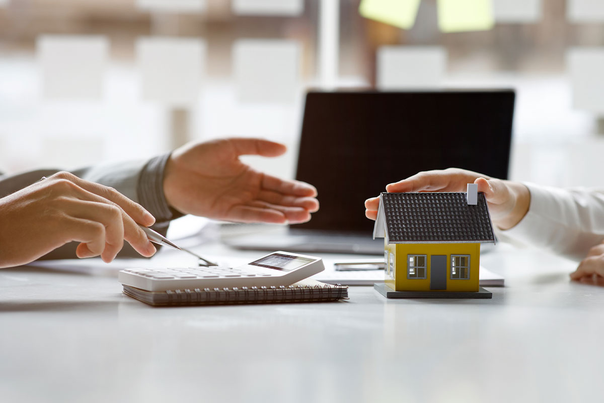 Real estate professionals reviewing documents at a desk with a calculator and a small house model